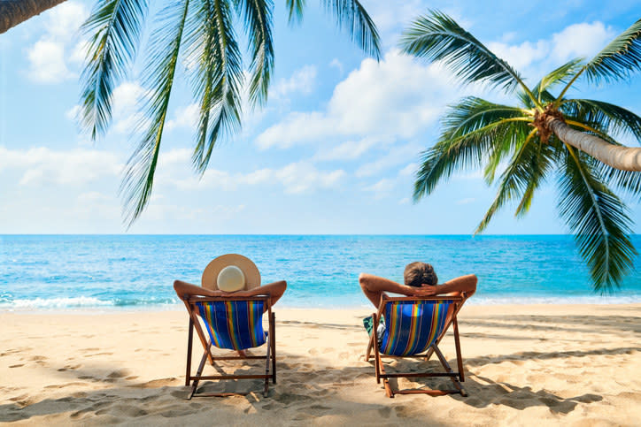 Two people in lounge chairs on a beach with their arms behind their back