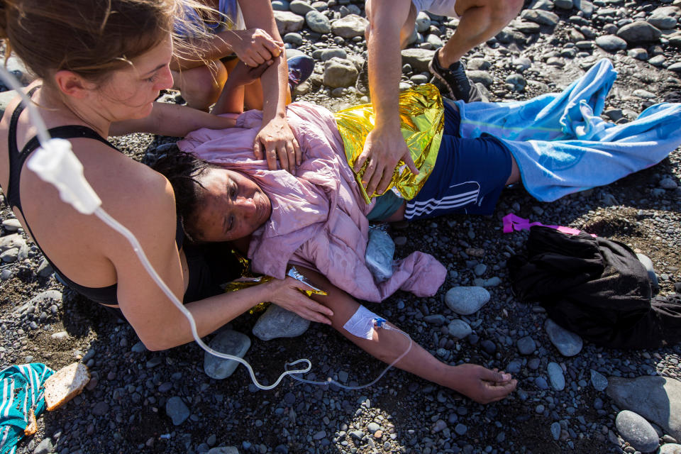 Beachgoers assist a woman, who is hooked up to an IV, after she landed with a group in a dinghy.