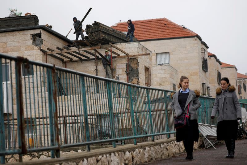 FILE PHOTO: Palestinian labourers perform construction work on a house as youths walk nearby in the Israeli settlement of Beitar Illit in the Israeli-occupied West Bank