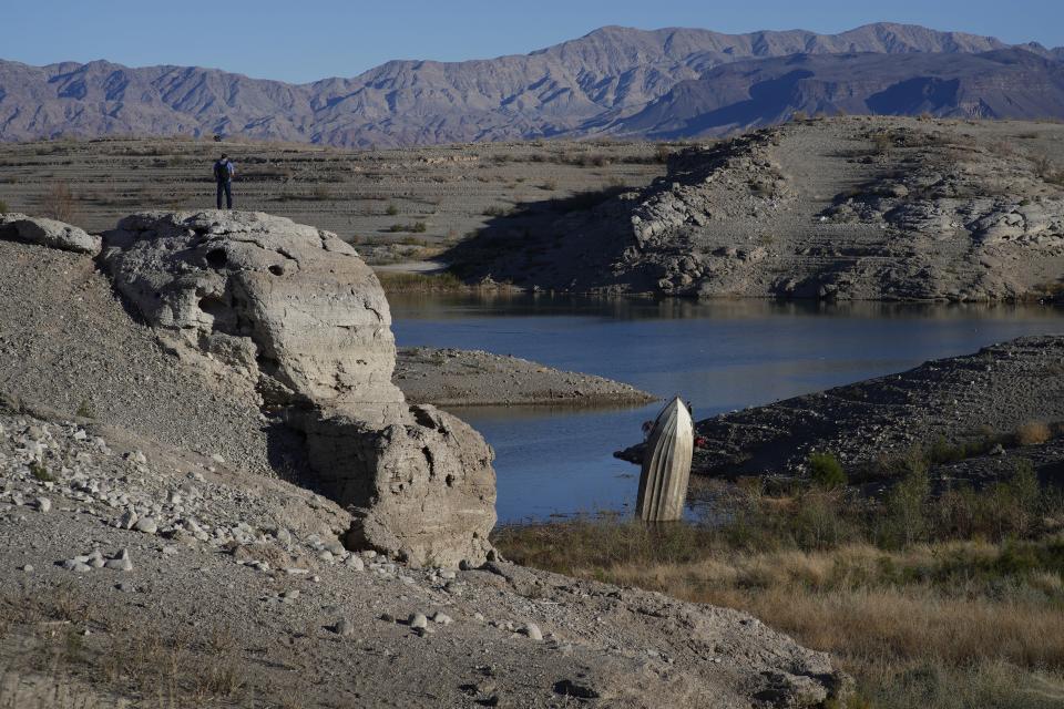 FILE - A man stands on a hill overlooking a formerly sunken boat standing upright into the air with its stern buried in the mud along the shoreline of Lake Mead at the Lake Mead National Recreation Area, Jan. 27, 2023, near Boulder City, Nev. A new study Thursday, May 18, 2023, says climate change’s hotter temperatures and society’s diversion of water have been shrinking the world’s lakes, including Lake Mead, by trillions of gallons of water a year since the early 1990s. (AP Photo/John Locher, File)