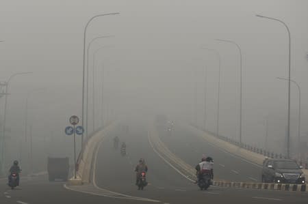 Motorists drive on the road as smoke covers the city due to the forest fire in Palembang