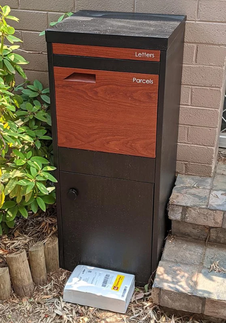 Pictured is a package on the ground next to a mailbox. 