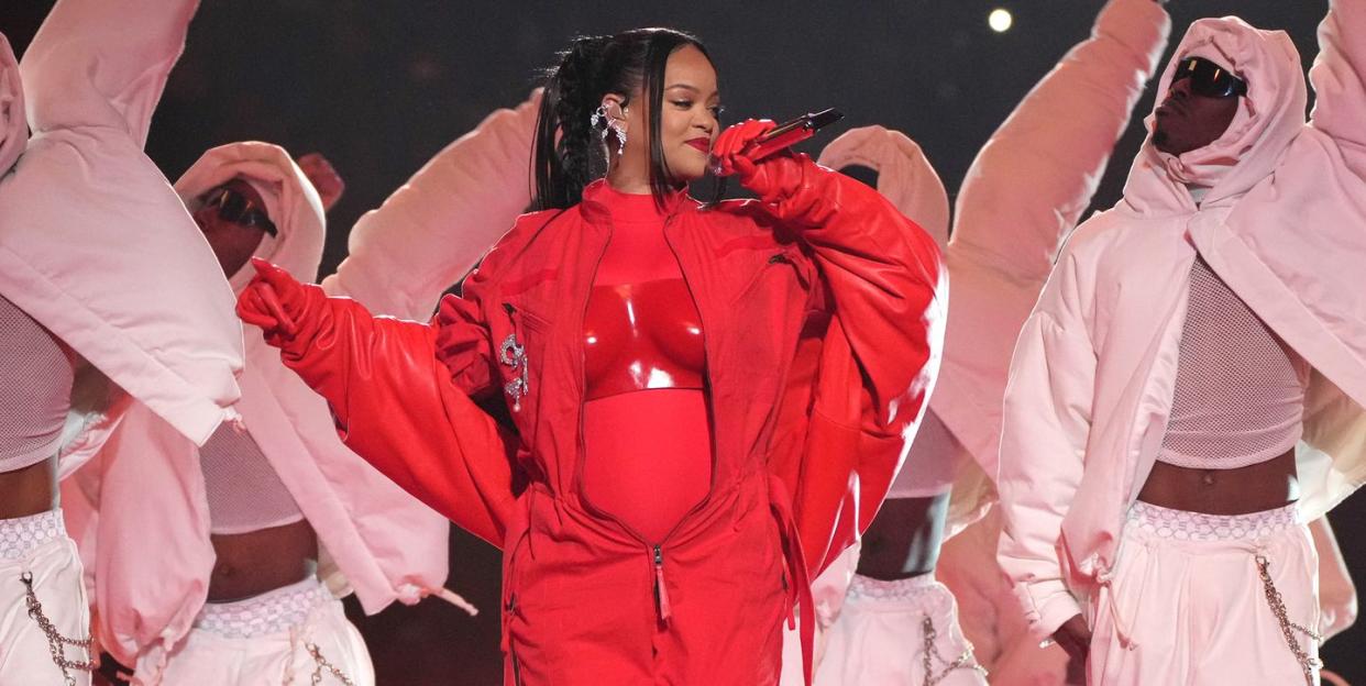 rihanna wearing a red outfit while singing into a microphone in front of several dancers wearing all white