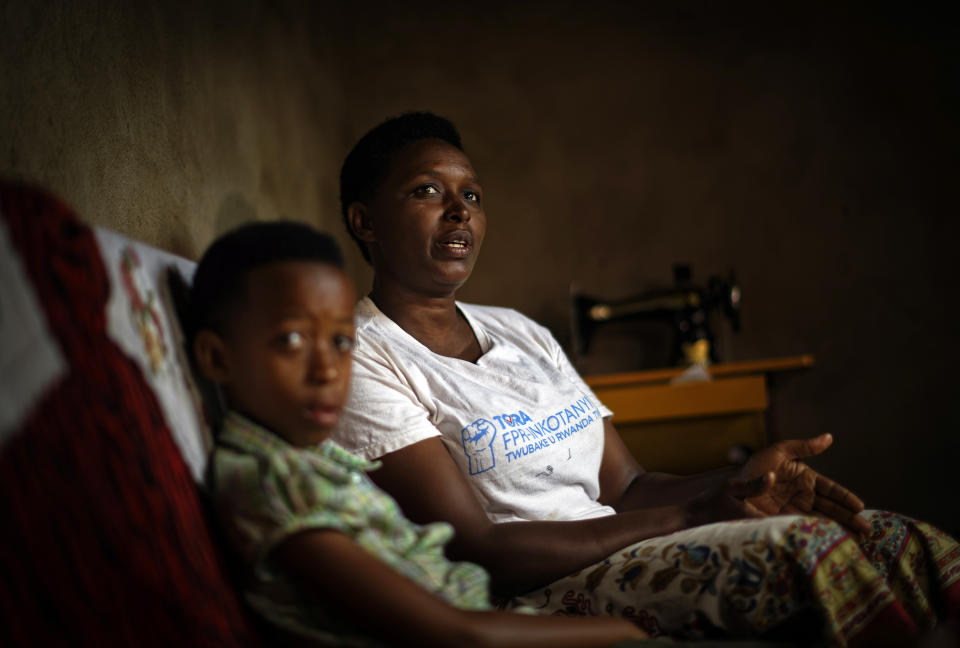In this photo taken Thursday, April 4, 2019, genocide survivor Jannette Mukabyagaju, 42, recounts her experience as her 8-year-old daughter Natasha Umutesi listens, in their home in the reconciliation village of Mbyo, near Nyamata, in Rwanda. Twenty-five years after the genocide the country has six "reconciliation villages" where convicted perpetrators who have been released from prison after publicly apologizing for their crimes live side by side with genocide survivors who have professed forgiveness. (AP Photo/Ben Curtis)