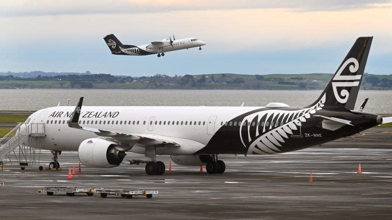 An Air New Zealand airline parked a remote parking spot with another ANZ plane taking off in the background.