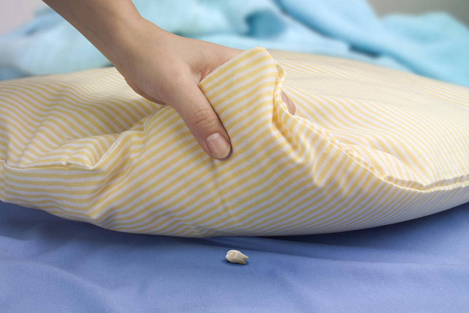 Woman's hand holds up pillow to show tooth placed for the Tooth Fairy.