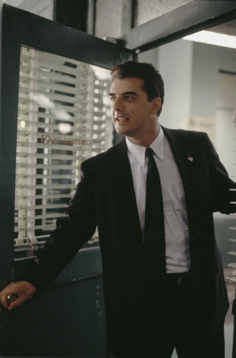 Chris Noth opening a door and leaning in while playing Detective Mike Logan in "Law & Order"