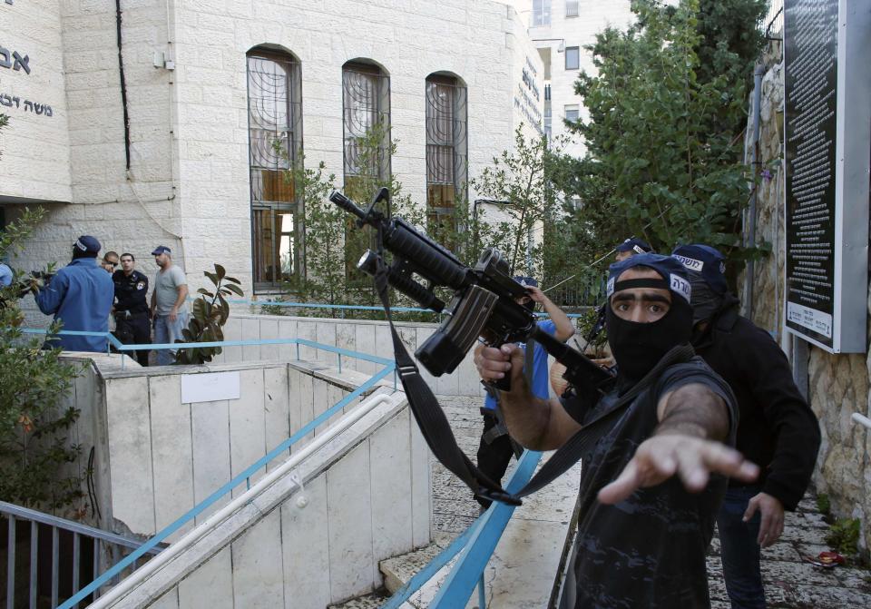 An Israeli police officer gestures as he holds a weapon near scene of an attack at a Jerusalem synagogue