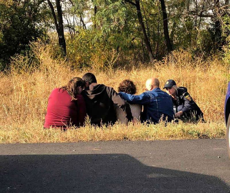 People react while sitting on the roadside near a crash site of the Ukrainian military Antonov An-26 aircraft outside Chuhuiv