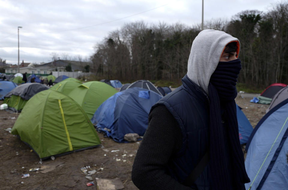 In this photo taken Tuesday, Jan.15, 2019, a migrant who pretends to be named Dariush, from Afghanistan, walks through tents in Calais, northern France, . Land, sea and air patrols are combing the beaches, dunes and frigid, murky coastal waters of northern France in a bid to end an unusual high-risk tactic by migrants, mostly Iranians: trying to sneak across the English Channel in rubber rafts. (AP Photo/Michel Spingler)
