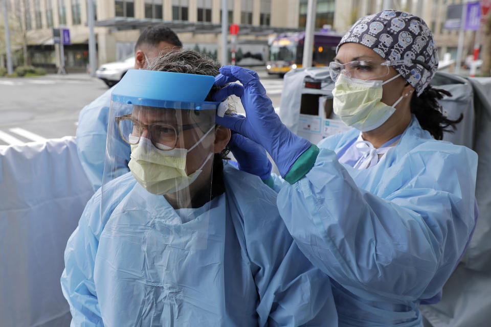 An emergency services nurse at Harborview Medical Center in Seattle helps a colleague put on a medical face shield prior to their shift in a triage tent used for arriving patients who have respiratory symptoms. (Photo: ASSOCIATED PRESS)