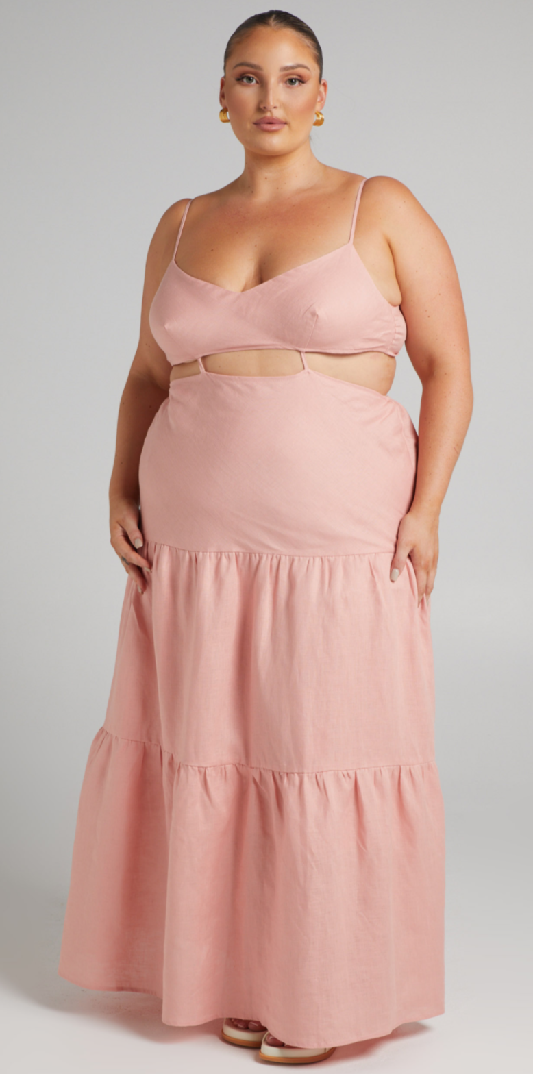 Curvy woman with dark hair tied back wears a pink tiered version of the SHOWPO Amalie the Label Rozelle Linen cut-out tie-back maxi dress - $149.95