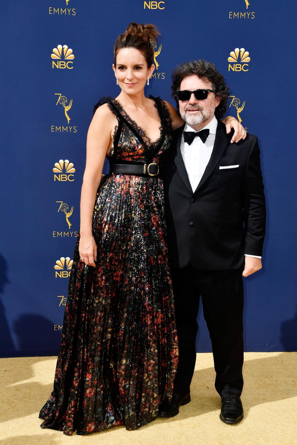 Tina Fey in a floor-length dark floral gown standing taller than Jeff Richmond in a dark sunglasses and a tuxedo.