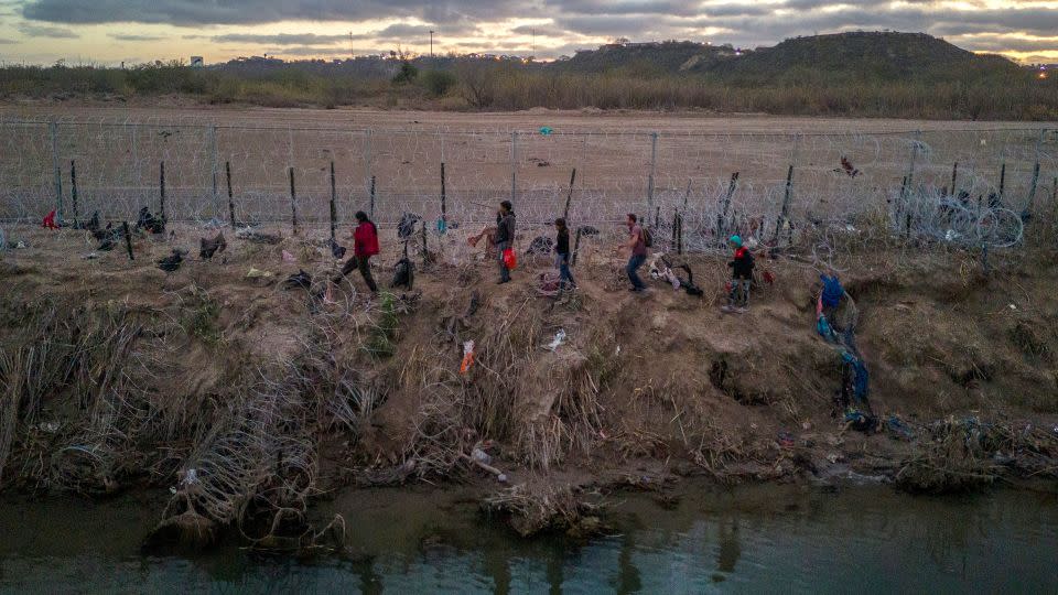 Migrants walk along razor wire after crossing the Rio Grande into the US on January 8 in Eagle Pass, Texas. - John Moore/Getty Images