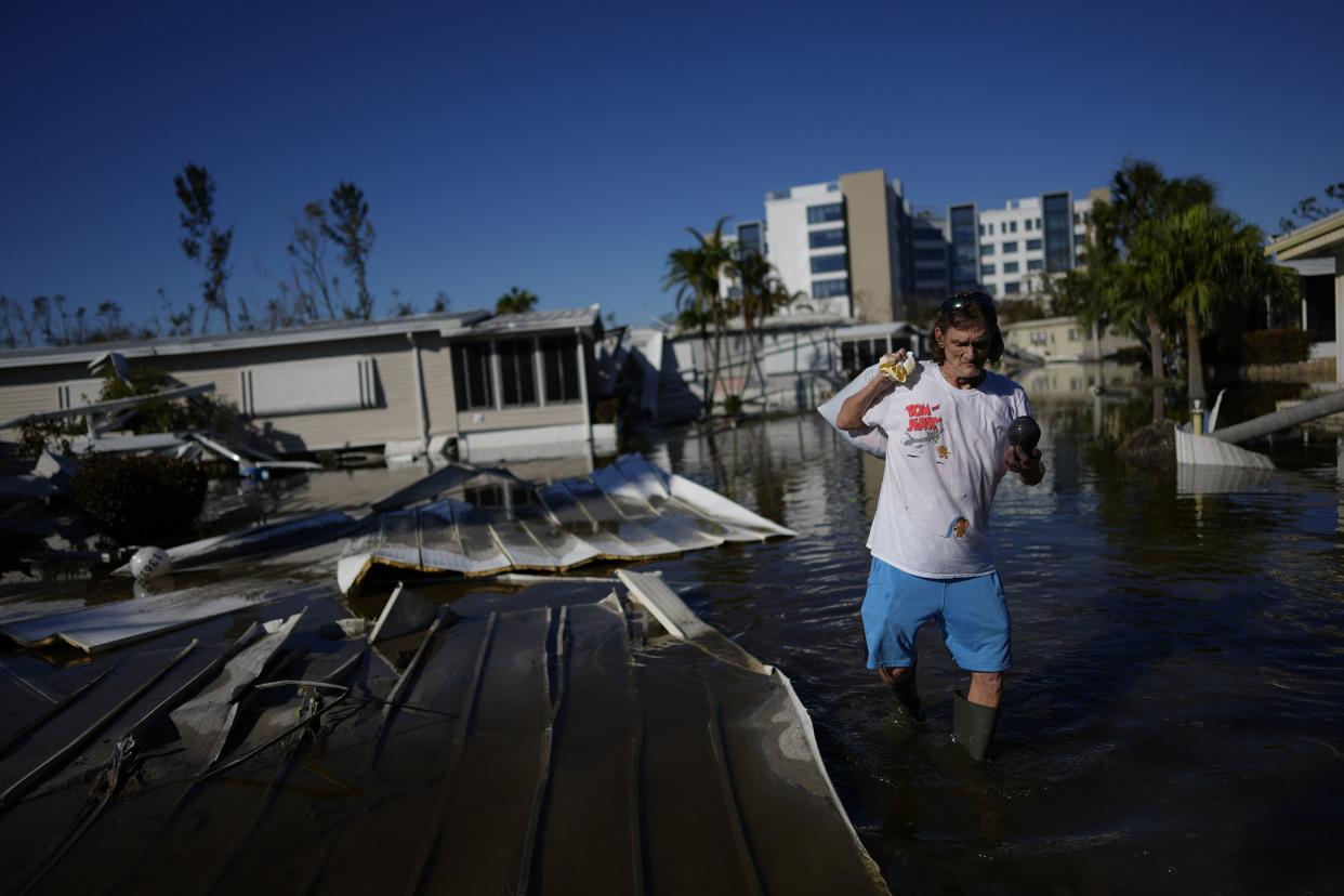 Dusty Hollar, 57, a cancer survivor who lives with chronic illness, carries the urn containing his father's ashes, as he recovers a few personal items from the mobile home that he shares with his 80-year-old mother in Sunshine Mobile Home Park, three days after the passage of Hurricane Ian, in Fort Myers, Fla., Saturday, Oct. 1, 2022. The family's home stayed on its foundations, unlike those of some of their neighbors, but flooding almost to the height of their ceiling destroyed most of their possessions and household items.