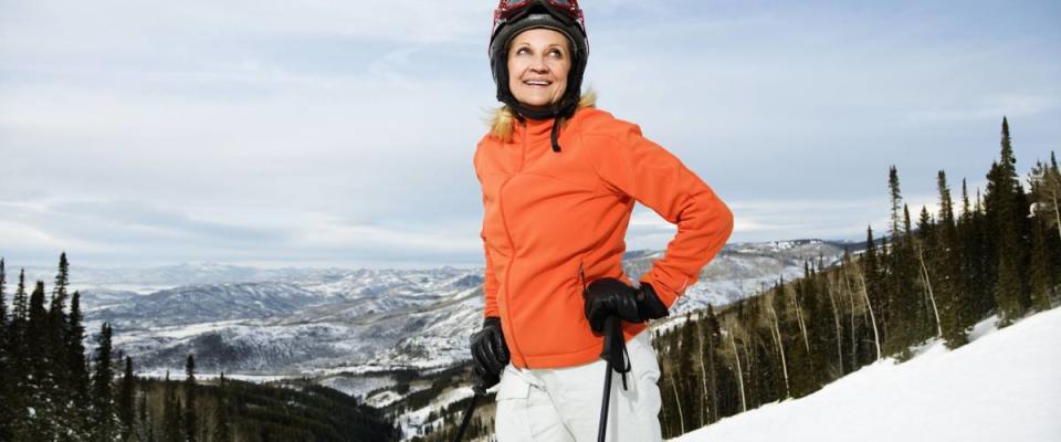 Smiling skier on ski slope in Colorado leaning on her poles with mountains in background. Horizontal shot.