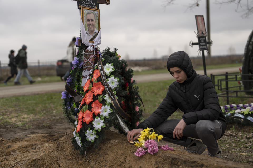 Yura Nechyporenko coloca una chocolatina en la tumba de su padre, Ruslan Nechyporenko, en el cementerio de Bucha, a las afueras de Kiev, Ucrania, el jueves 21 de abril de 2022. El joven sobrevivió a un intento de ejecución de soldados rusos, mientras que su padre murió, y ahora la familia pide justicia. (AP Foto/Petros Giannakouris)