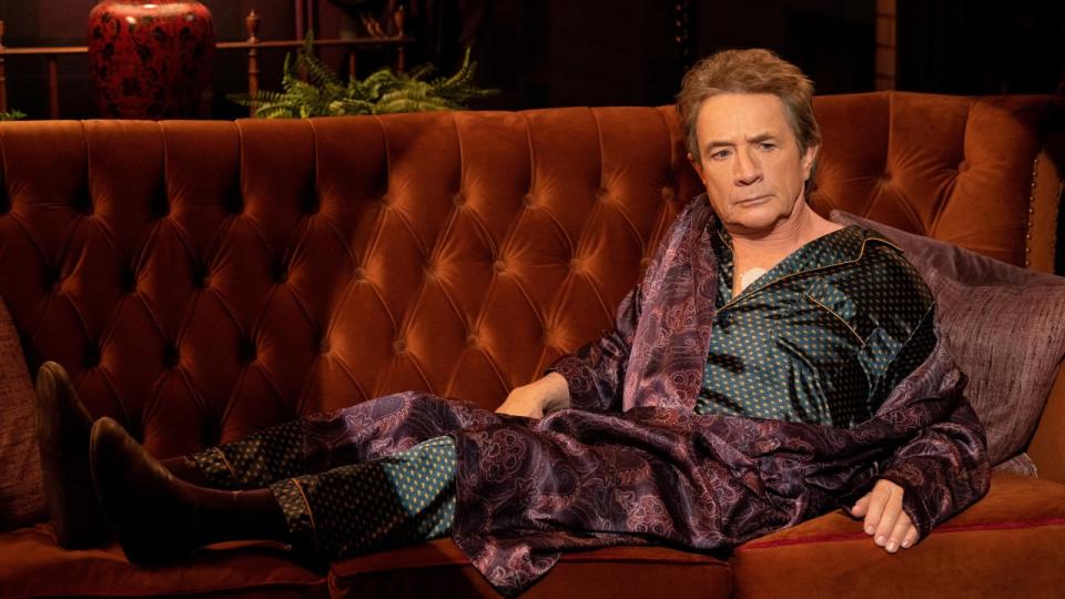 Martin Short sitting on a couch with a spotlight on him.