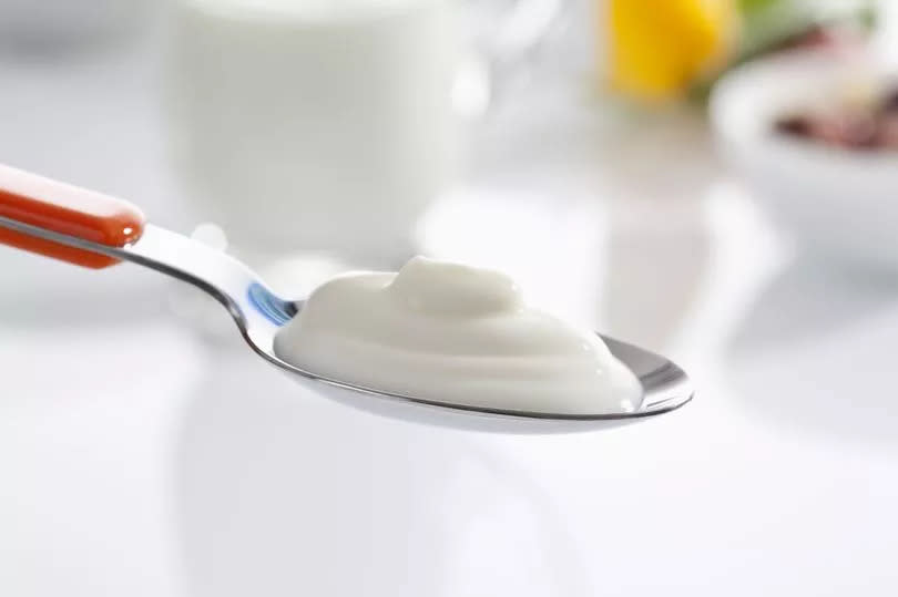 Spoon of yogurt against white background, close up