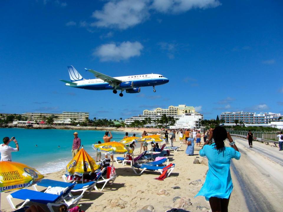 People on a beach with a large plane landing and hotels in the background on Sint Maarten.