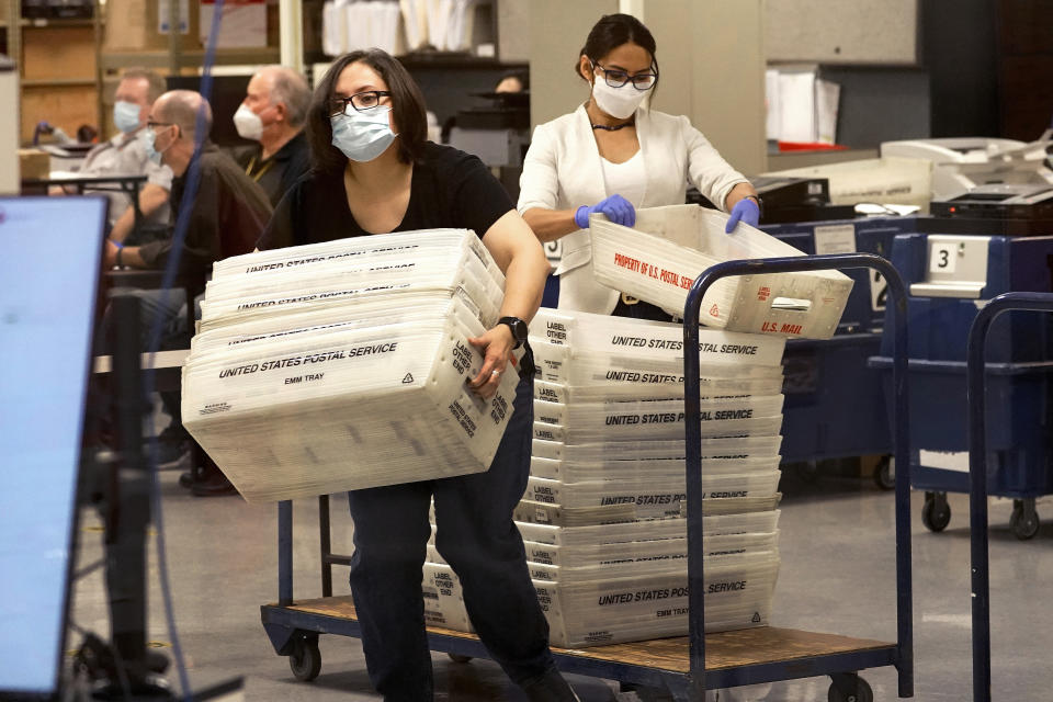 Arizona elections officials carry ballots in trays to be counted inside the Maricopa County Recorder's Office, Friday, Nov. 6, 2020, in Phoenix. (AP Photo/Matt York)