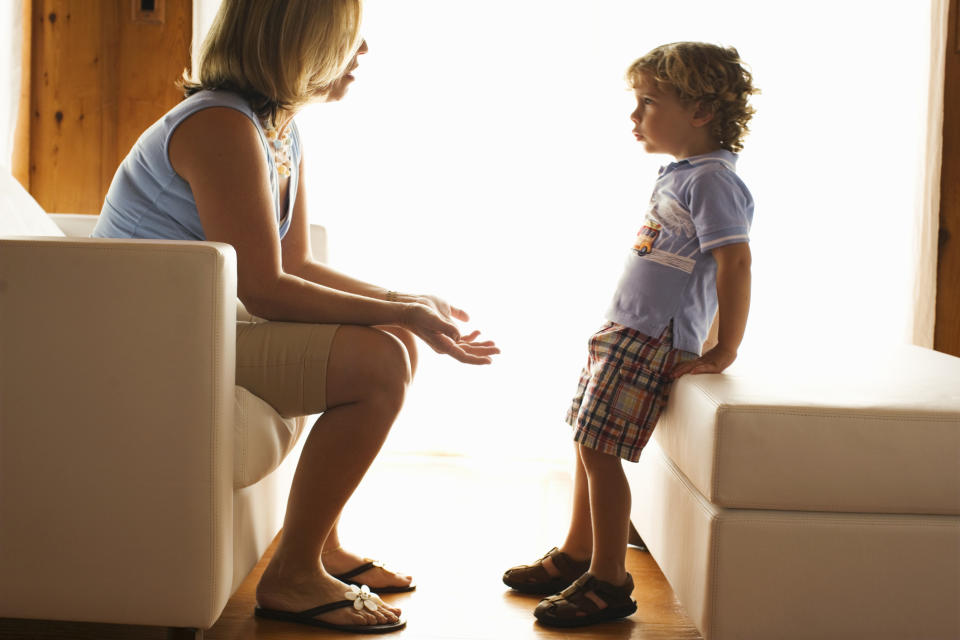 Woman seated talking to a young child standing close by, indoors, facing each other