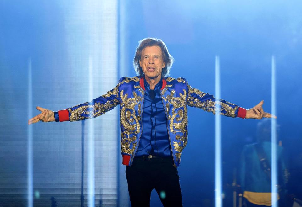 mick jagger stands on a stage with his arms outstretched as his sides