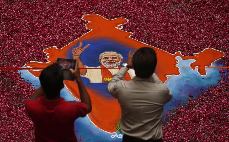 FILE- In this May 16, 2014 file photo, Indians take photographs of a portrait of Bharatiya Janata Party (BJP) leader Narendra Modi, with an outline of the India map made with colored powder and surrounded by rose petals, in Gandhinagar, Gujarat state, India. Modi, who became a Hindu nationalist before he was 10 years old, has upended life in India’s only Muslim-majority state, flexing those nationalist muscles for his millions of followers. (AP Photo/Saurabh Das, File)