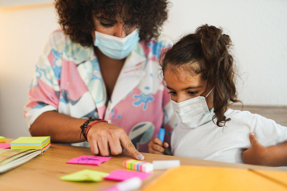 Mother doing home schooling with child while wearing surgical face mask for coronavirus