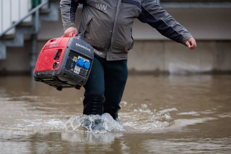 A man carries an electricity generator to a house that is standing in the water. The water level of the Weser has risen significantly over the past few days. Friso Gentsch/dpa