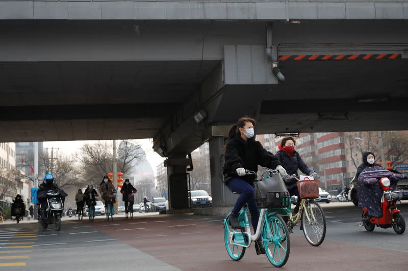 People wearing face masks ride bicycles and scooters on the street, as the country is hit by an outbreak of the new coronavirus, in Beijing