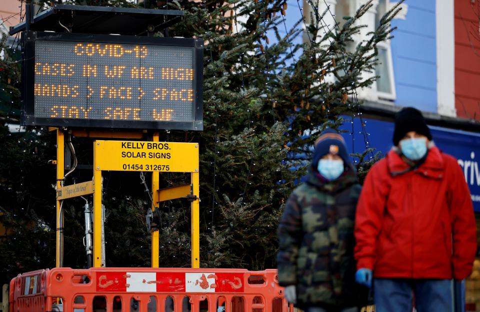 Pedestrians wearing a face mask or covering due to the COVID-19 pandemic, walk past an electronic COVID-19 information sign in Walthamstow in north east London, on December 15, 2020. - Two leading British medical journals urged the government Tuesday to scrap plans to ease coronavirus restrictions over Christmas, warning it would be "another major error that will cost many lives". The British capital faces tougher Covid-19 measures within days, the UK government said on Monday, with a new coronavirus variant emerging as a possible cause for rapidly rising infection rates. (Photo by Tolga Akmen / AFP) (Photo by TOLGA AKMEN/AFP via Getty Images)