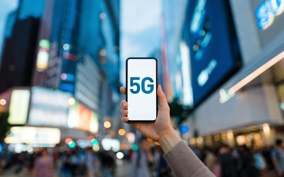 Woman's hand using smartphone against illuminated financial district in the city, with the concept of 5G communications technology