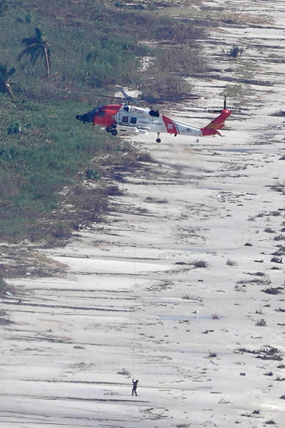 A Coast Guard helicopter hovers over a man on the beach in the aftermath of Hurricane Ian, Thursday, Sept. 29, 2022, on Sanibel Island, Fla. (AP Photo/Wilfredo Lee)