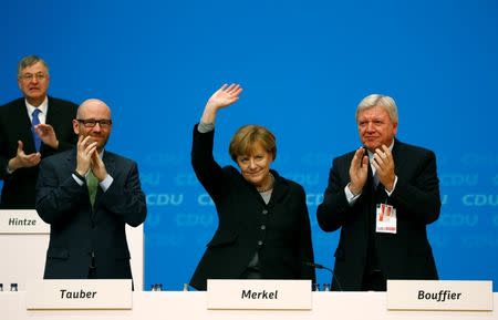 German Chancellor Angela Merkel and leader of the Christian Democratic Union (CDU) acknowledges applause after her keynote speech, while standing next to CDU secretary general Peter Tauber CDU deputy head and Hesse's state Premier Volker Bouffier (R) during the party congress in Karlsruhe, Germany December 14, 2015. REUTERS/Kai Pfaffenbach