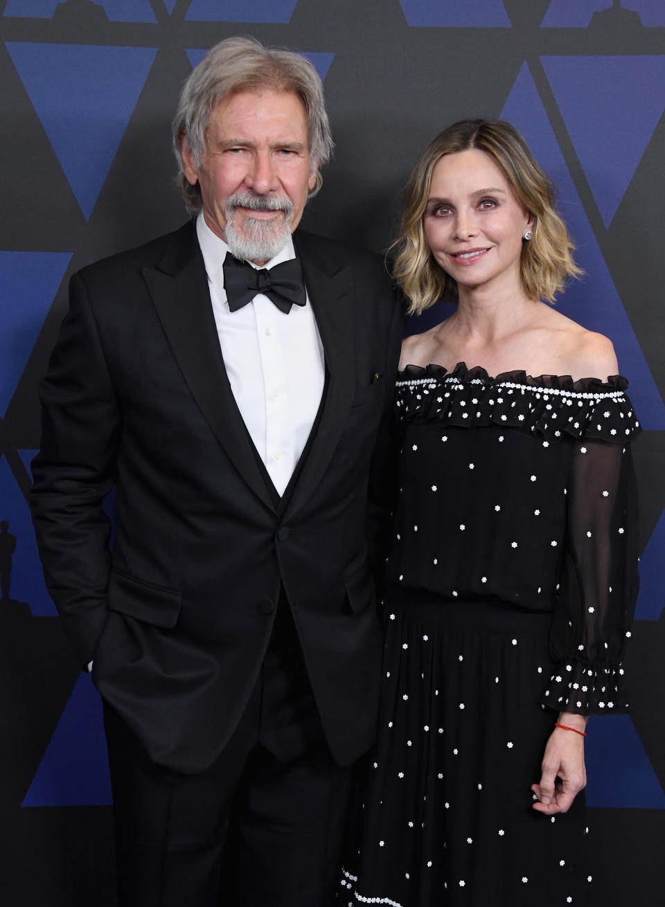 Two celebrities in formal wear, a man in a tuxedo and a woman in a polka-dot dress with detailed details.