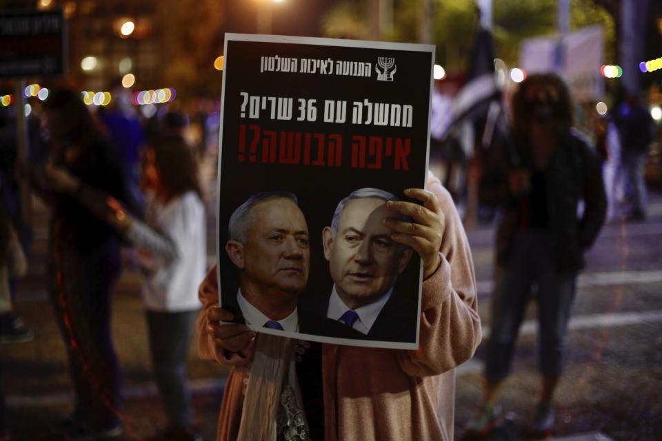A woman holds a poster of Israeli Prime Minister Benjamin Netanyahu, right, and Benny Gantz, left, that read 'a government with 36 ministers? Where is the shame?' during a protest against the government and the corruption, at Rabin square, in Tel Aviv, Israel, Saturday, May 2, 2020. Several thousand Israelis took to the streets on Saturday night, demonstrating against Prime Minister Benjamin Netanyahu's new coalition deal with his chief rival a day before the country's Supreme Court is to begin debating a series of legal challenges to the agreement.(AP Photo/Ariel Schalit)