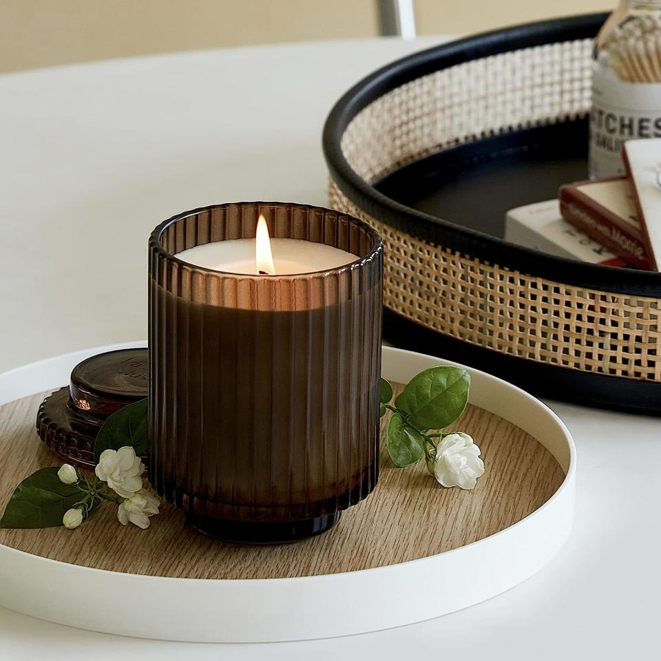 brown ribbed glass candle lit on a trinket tray with a similar rattan tray nearby