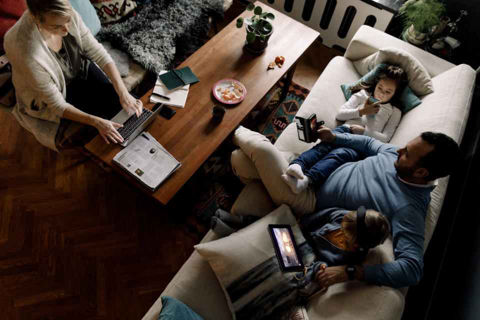 A high-angle view of family using various technologies in living room, in relation to people testing positive for Covid at home.