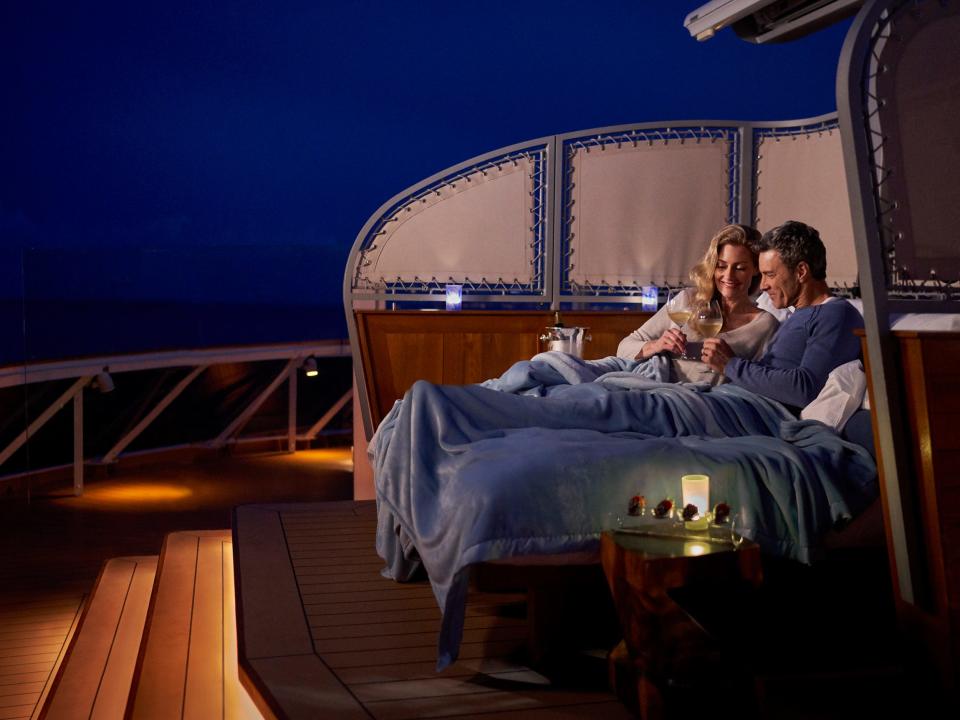 A couple sharing an evening drink while sitting together under a blanket on a deck of The World.