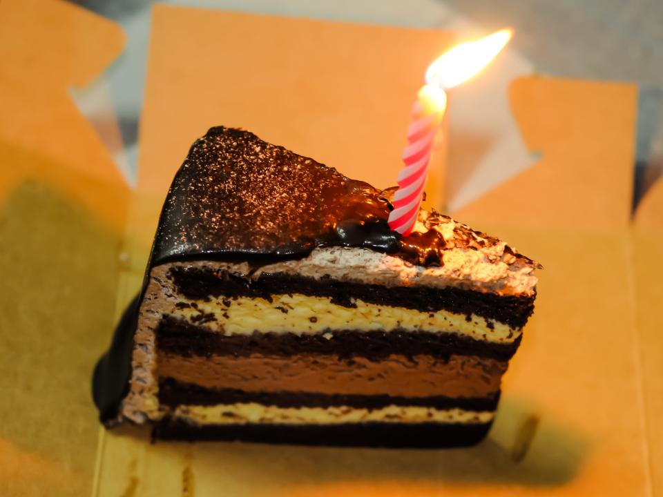 A slice of a birthday cake with a lit candle on it