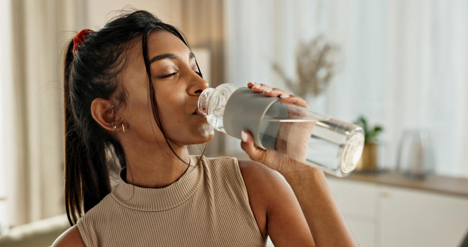 Drinking water, yoga or Indian woman in home with health, fitness or wellness for natural hydration.  Thirsty female person, tired or healthy girl with liquid bottle after pilates for detox or relax
