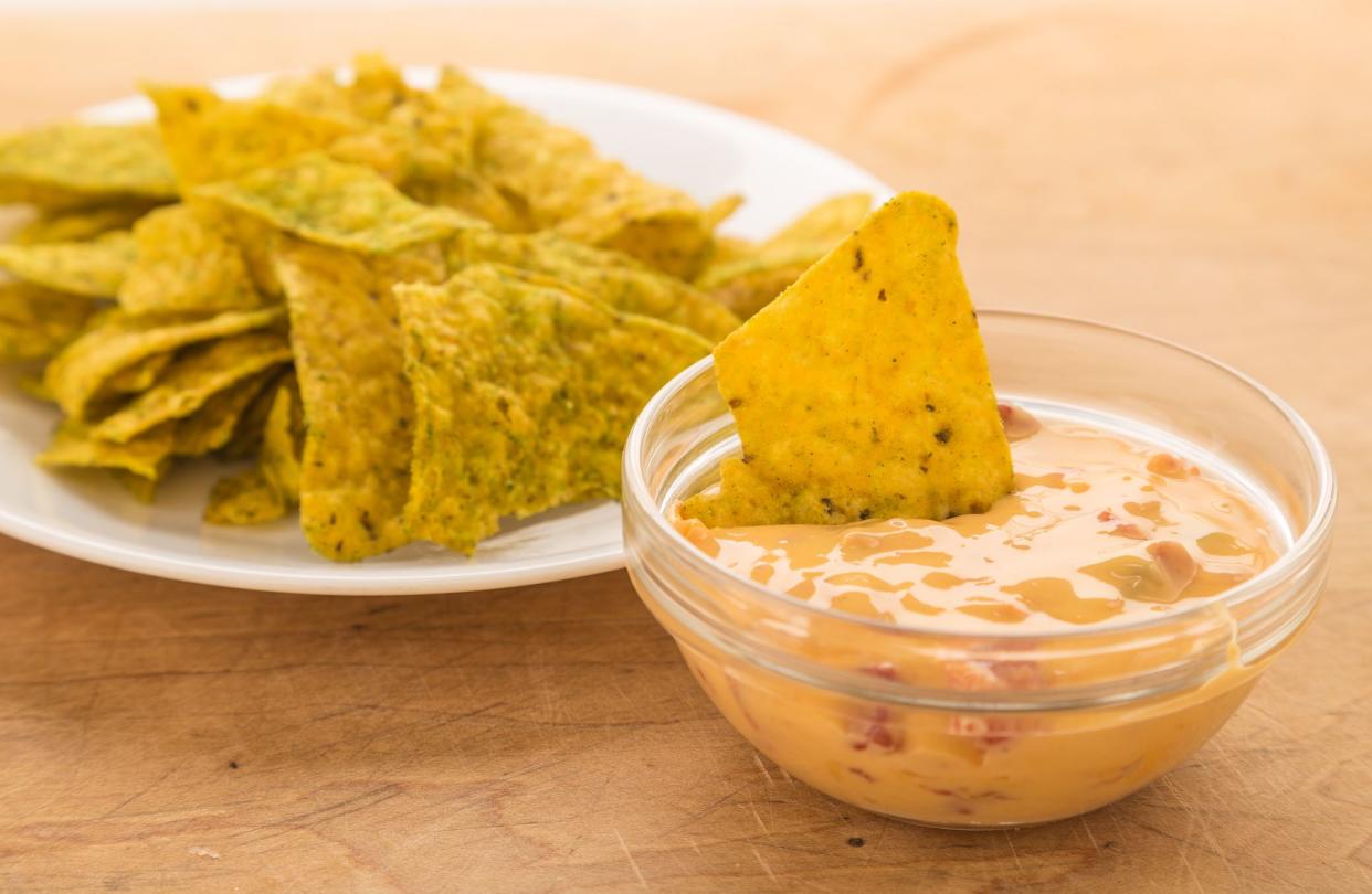 Dipping spicy jalapeno tortilla chips in creamy chili con queso dip in clear glass bowl.