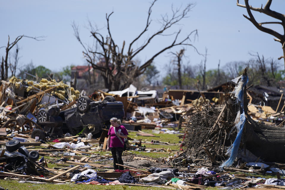 FILE - A woman walks near an uprooted tree, a flipped vehicle and debris from homes damaged by a tornado, Monday, March 27, 2023, in Rolling Fork, Miss. President Joe Biden on Friday will visit a Mississippi town ravaged by a deadly tornado even as a new series of severe storms threatens to rip across the Midwest and South. (AP Photo/Julio Cortez, File)