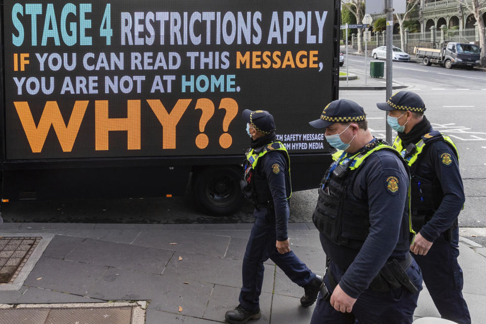 Victorian protective service officers are seen walking on patrol past a sign to urge people to stay home during lockdown. Source: AP