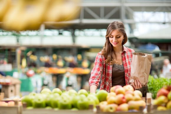 A young woman picks out produce at a grocery store.