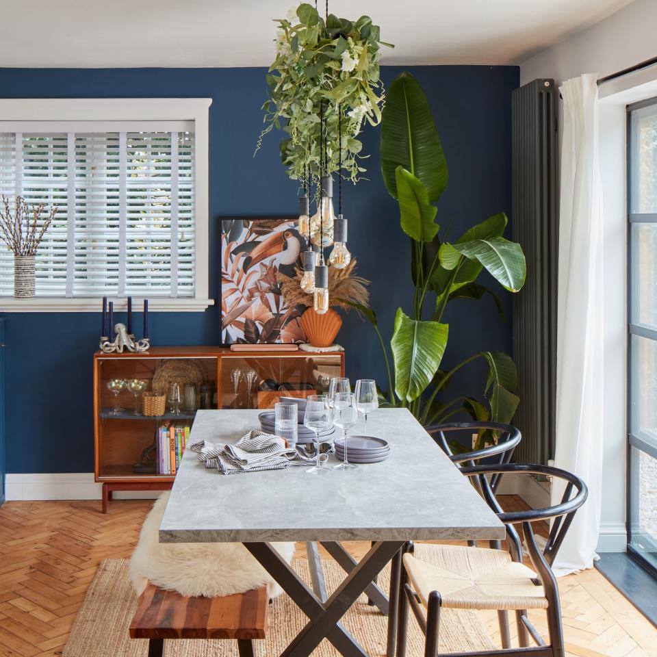 blue navy walled dining area with white table, foliage and wooden storage unit