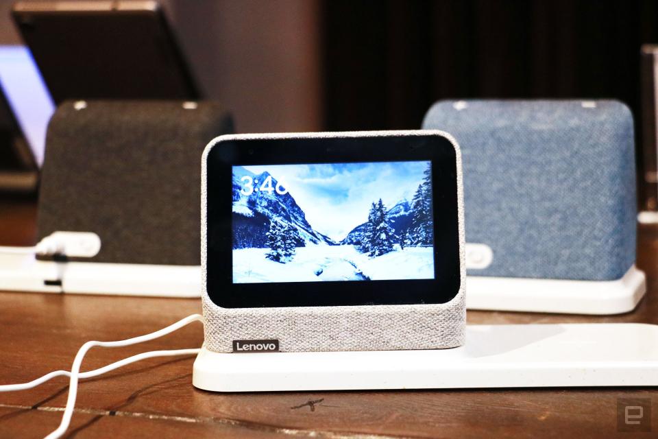 <p>A gray Lenovo Smart Clock 2 on a wireless charging dock with its screen facing the camera. In the background are a black and a blue Smart Clock 2 on the left and right respectively.</p>
