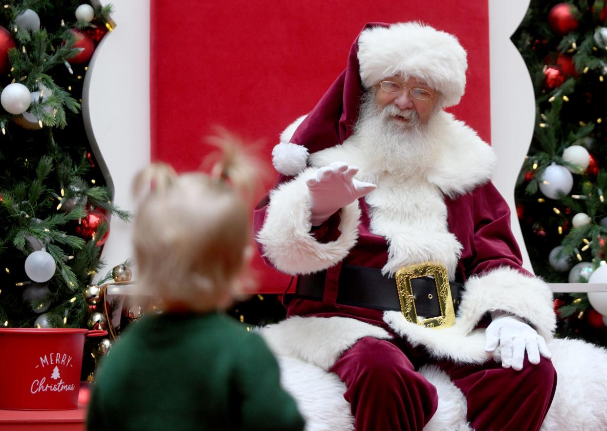Ella Pendleton, 1, of Canton makes a cautious approach with a wave from Santa, with help from Bernie Roberts of Akron, at Belden Village Mall.
