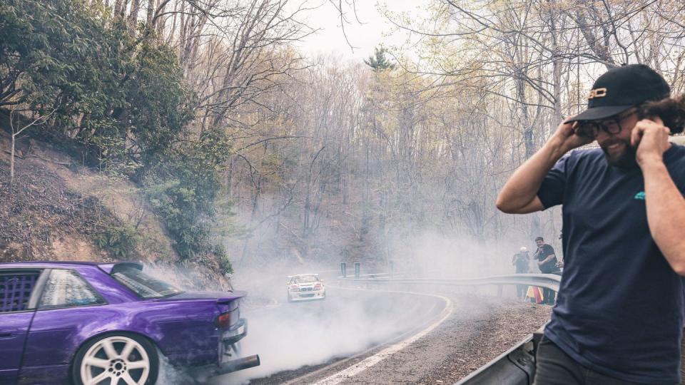 a man taking a picture of a car on a road with smoke coming out of it